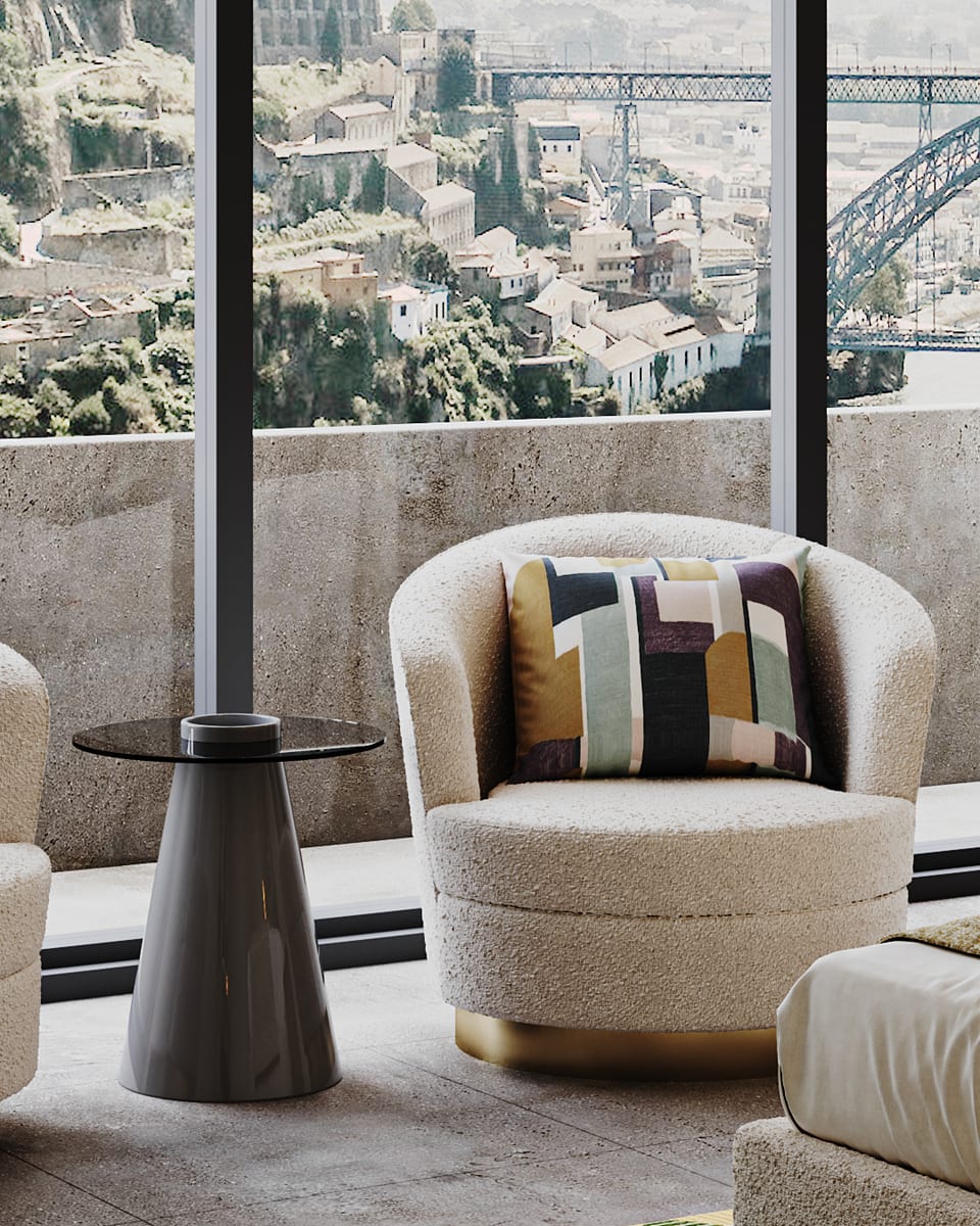 Cadeirão em bouclé creme com base dourada e almofada geométrica, junto ao vidro com vista sobre o rio